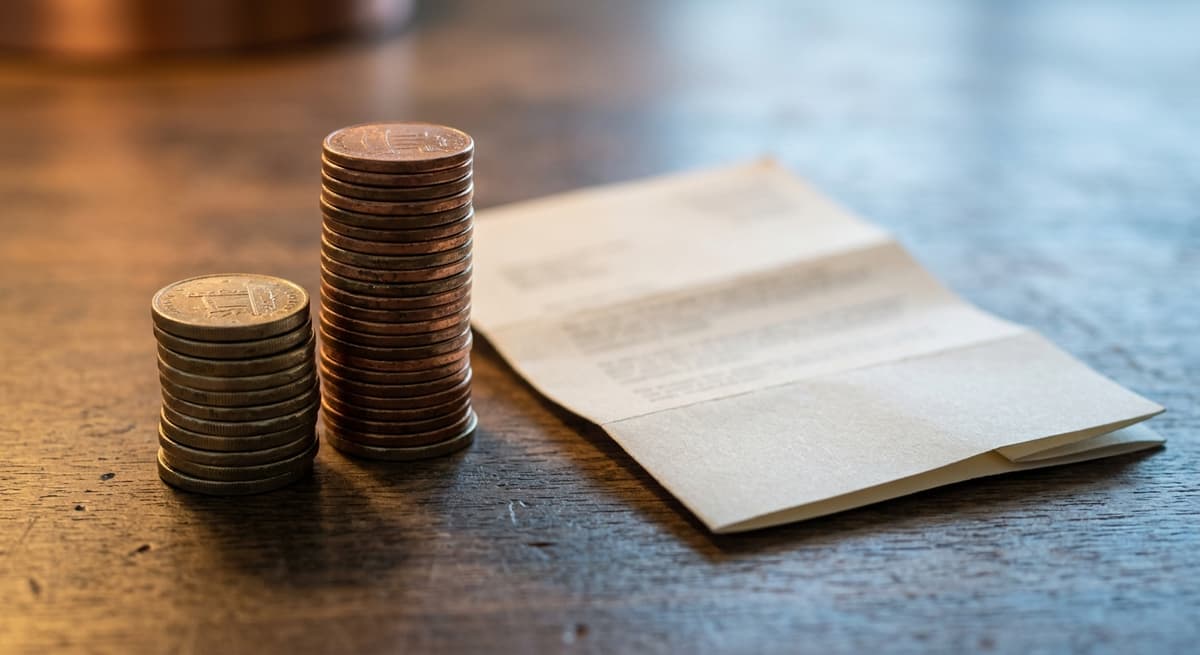 dos pilas de monedas de diferentes alturas sobre un escritorio junto a un documento doblado