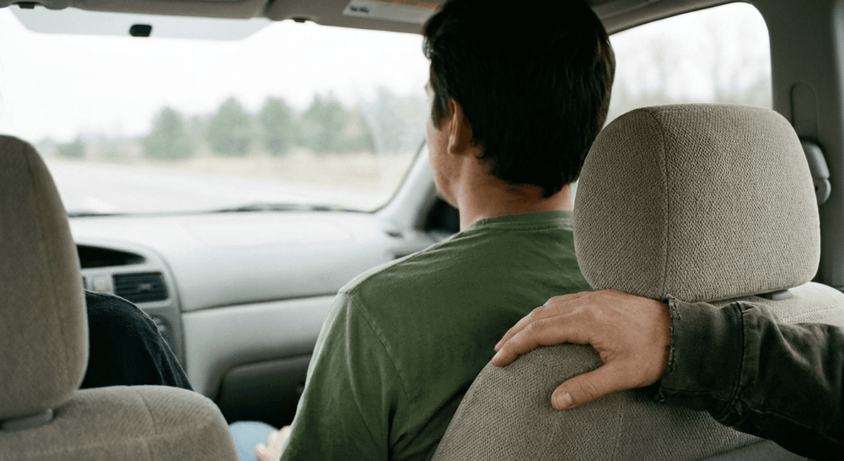 Vista desde el asiento trasero de un auto: el conductor de espaldas y la mano de un pasajero sobre el reposacabezas