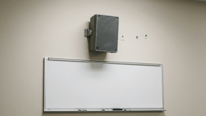 Altavoz del sistema de megafonia escolar de Nevada montado en la pared de un salon de clases sobre la pizarra blanca