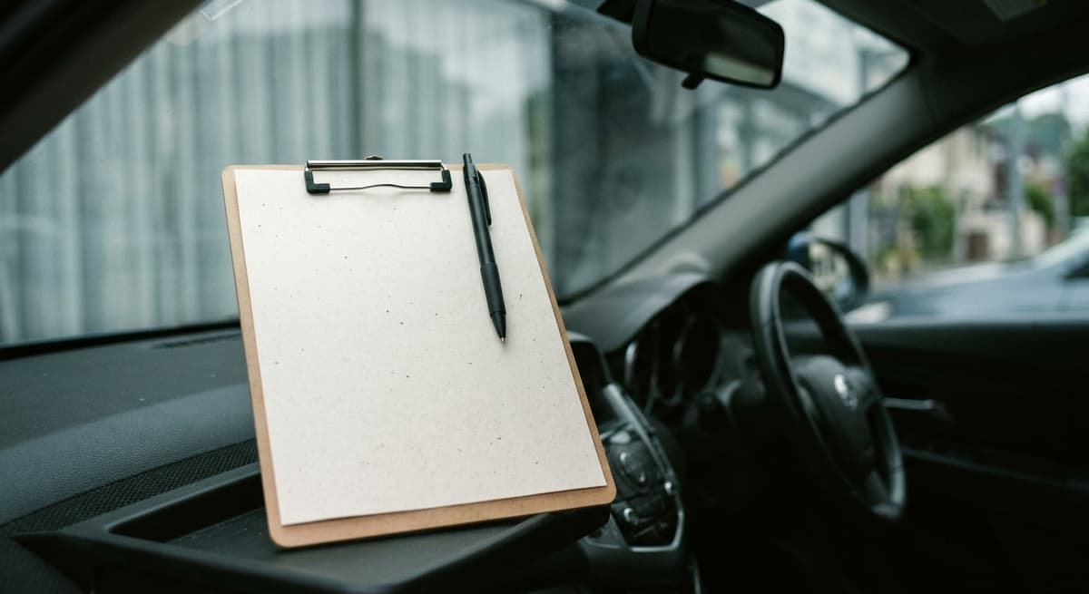 a printed blank form on a clipboard with a pen clipped to the top, resting on a car dashboard